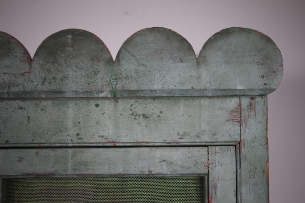 A large Georgian pine food safe in distressed sage green paint featuring a scalloped top pediment and wire mesh double doors. View IV