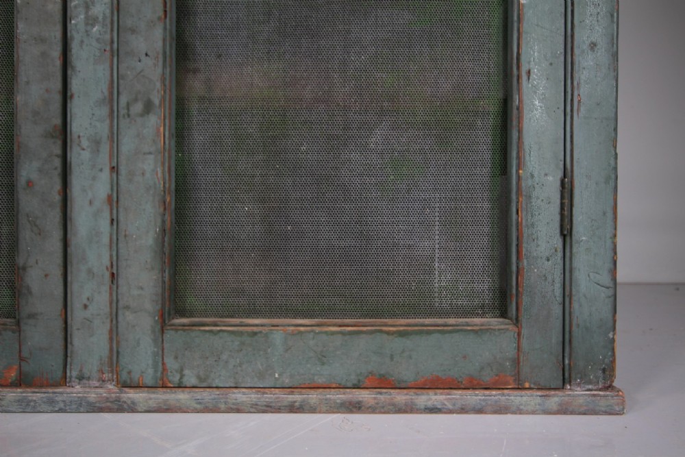 A large Georgian pine food safe in distressed sage green paint featuring a scalloped top pediment and wire mesh double doors. View V