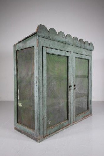 A large Georgian pine food safe in distressed sage green paint featuring a scalloped top pediment and wire mesh double doors.