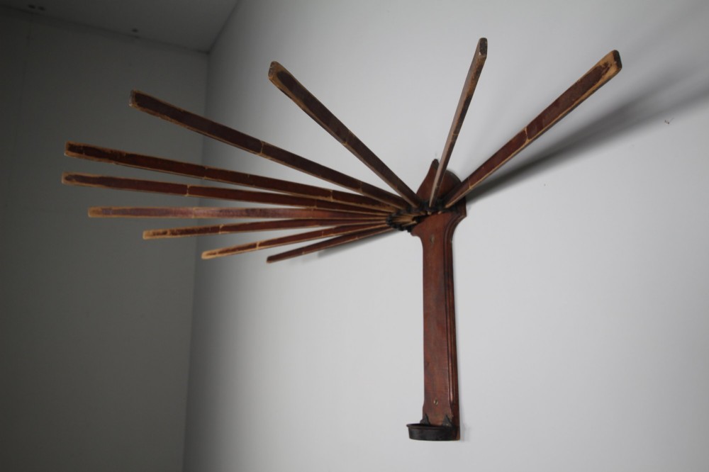 An antique wall-mounted wooden clothes dryer featuring multiple moveable laths fanning out from a central dark wood backplate. View II