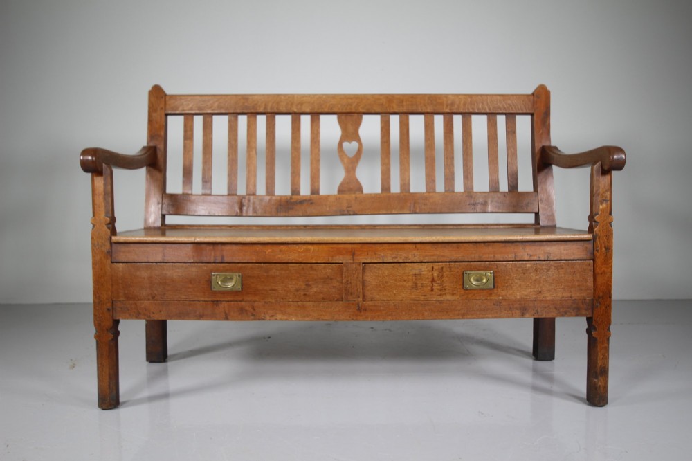 A nineteenth-century oak hall bench with a slatted back featuring a central pierced heart motif, scrolled arms, and two drawers with flush brass handles beneath the seat. View II