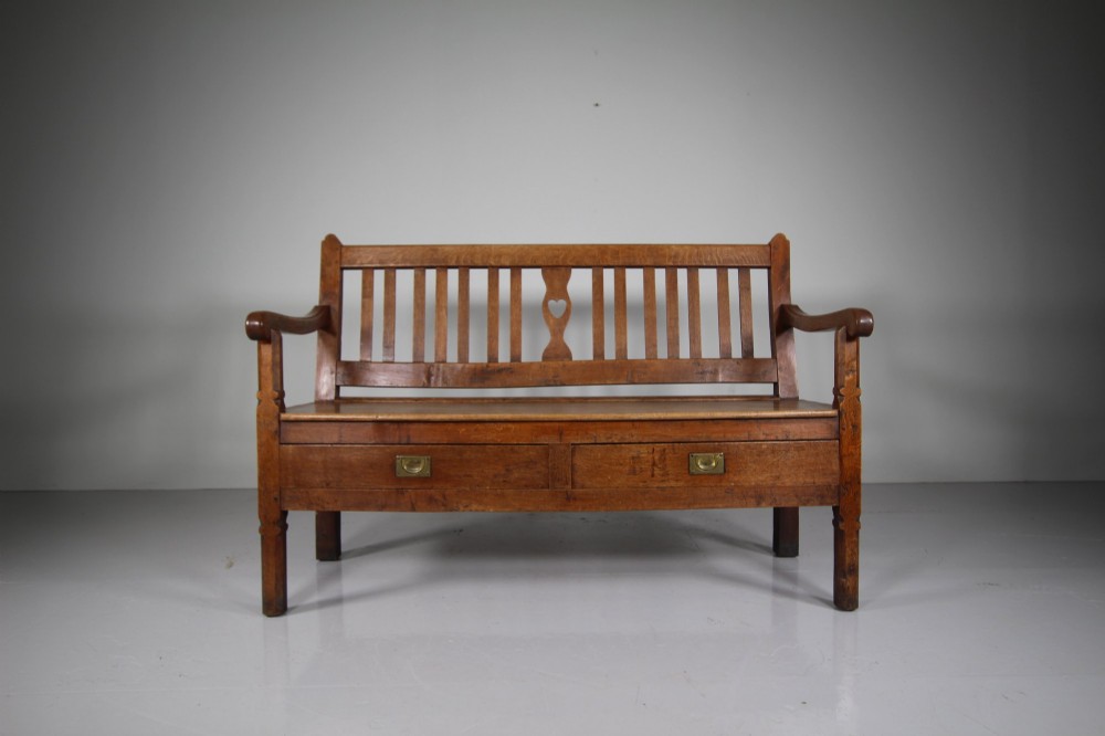 A nineteenth-century oak hall bench with a slatted back featuring a central pierced heart motif, scrolled arms, and two drawers with flush brass handles beneath the seat. View III