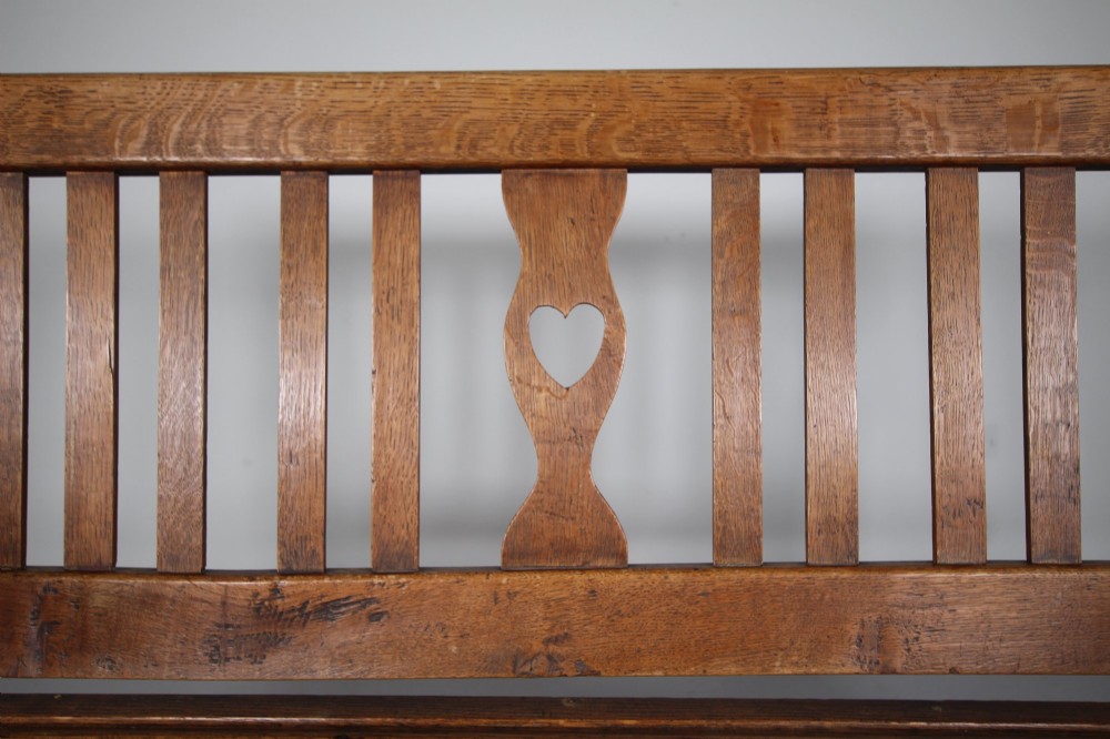 A nineteenth-century oak hall bench with a slatted back featuring a central pierced heart motif, scrolled arms, and two drawers with flush brass handles beneath the seat. View IV