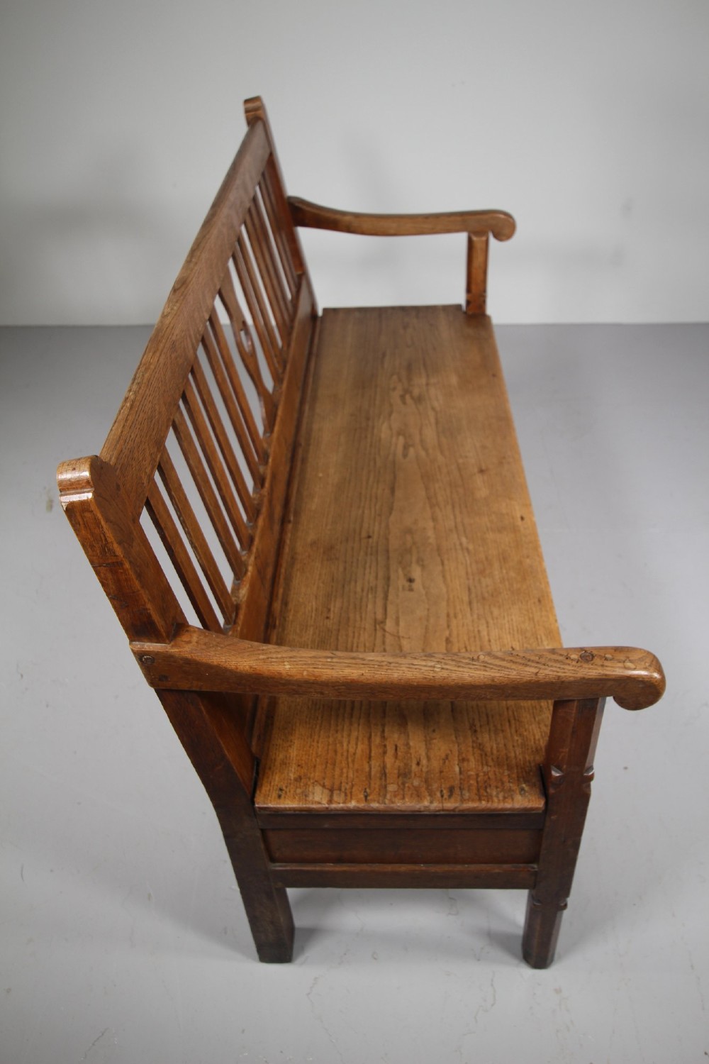 A nineteenth-century oak hall bench with a slatted back featuring a central pierced heart motif, scrolled arms, and two drawers with flush brass handles beneath the seat. View IX