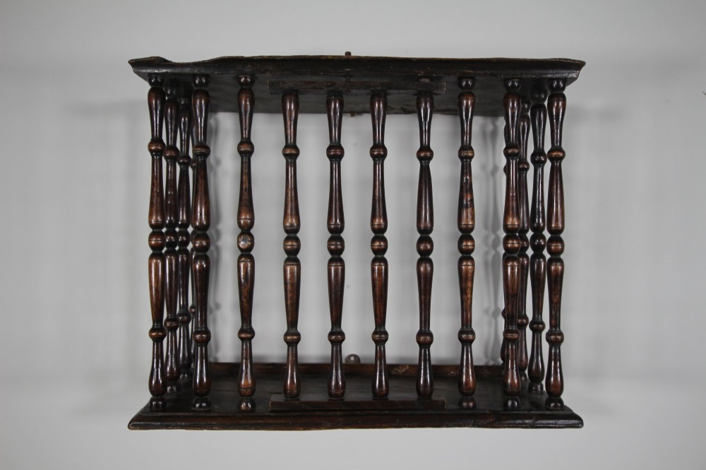A 17th-century dark oak wall-mounted livery cupboard featuring a rectangular frame enclosing closely set turned wooden spindles on all open sides.