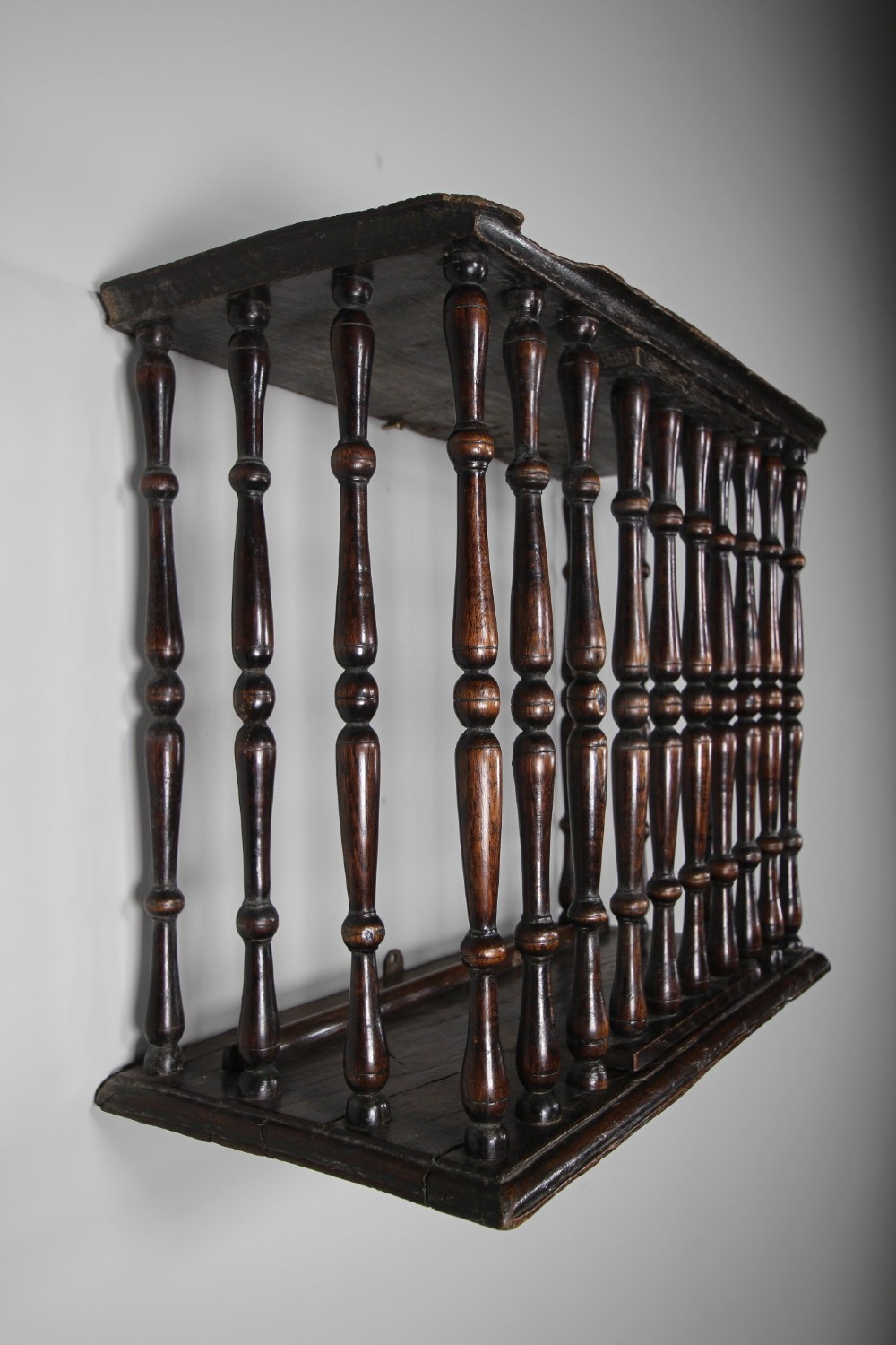 A 17th-century dark oak wall-mounted livery cupboard featuring a rectangular frame enclosing closely set turned wooden spindles on all open sides. View VIII