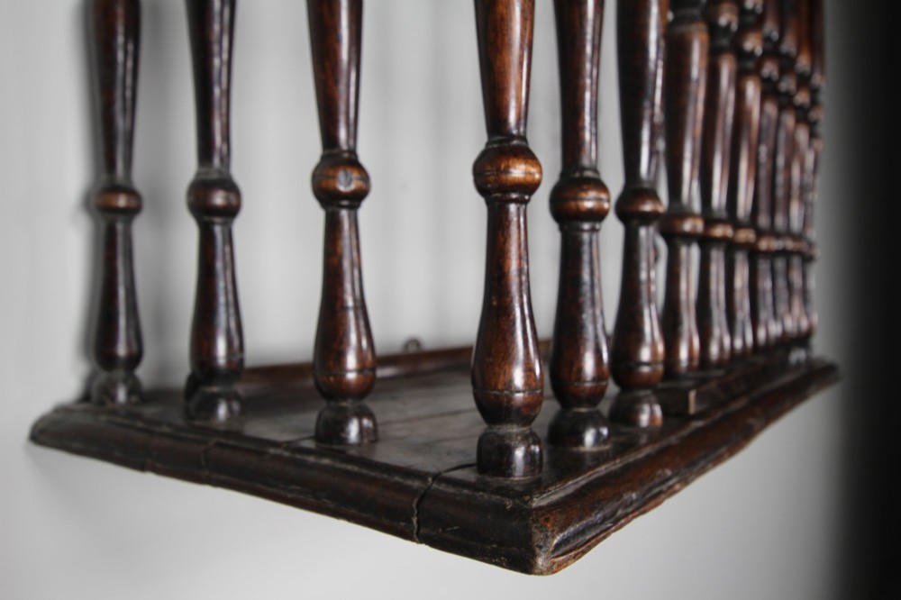 A 17th-century dark oak wall-mounted livery cupboard featuring a rectangular frame enclosing closely set turned wooden spindles on all open sides. View X