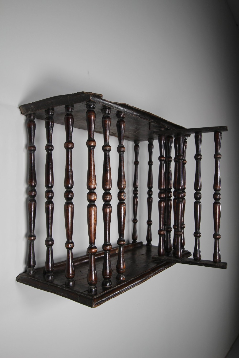 A 17th-century dark oak wall-mounted livery cupboard featuring a rectangular frame enclosing closely set turned wooden spindles on all open sides. View XI