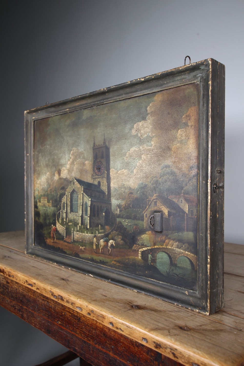 An 18th-century oil painting on tin depicting a church landscape with integrated mechanical clock hands and a visible waterwheel mechanism, enclosed in a dark wooden frame. View II