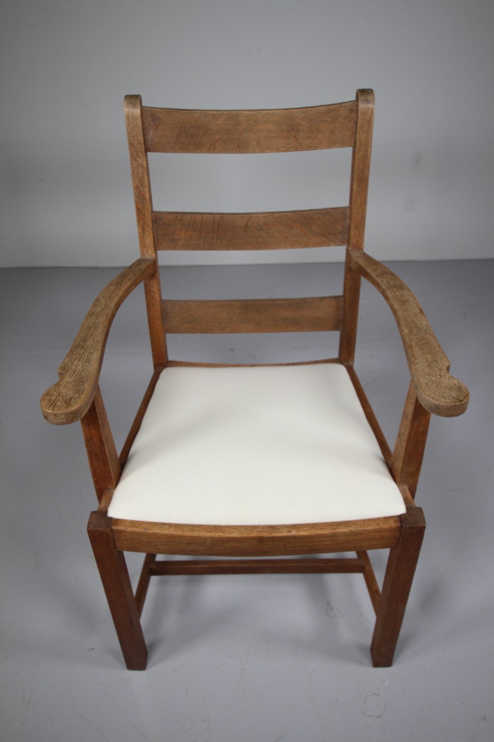 An Arts and Crafts solid oak armchair featuring a ladderback design, flat armrests, and an upholstered cream seat cushion. View II