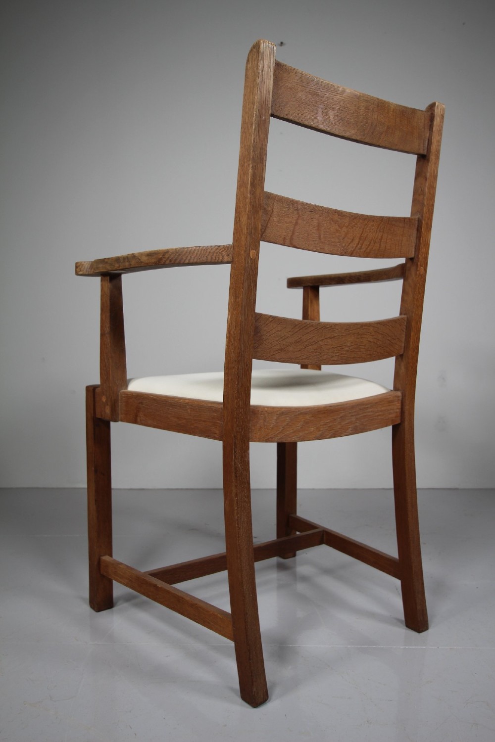 An Arts and Crafts solid oak armchair featuring a ladderback design, flat armrests, and an upholstered cream seat cushion. View III