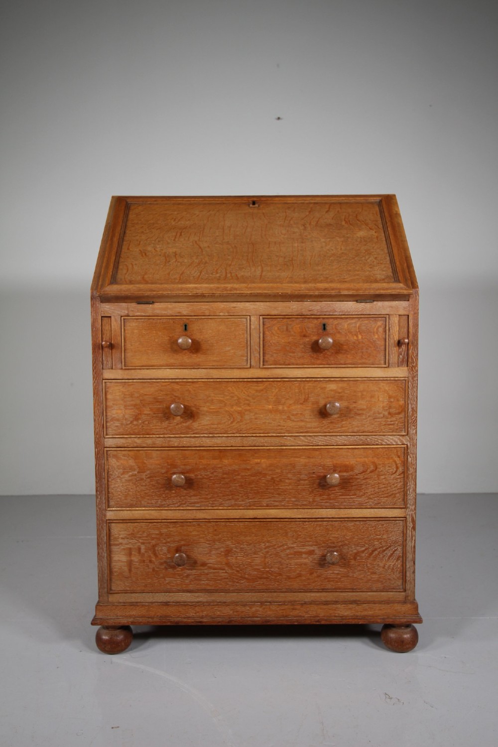 A 1920s oak writing bureau featuring a sloped fall-front desk above four drawers with turned wooden knobs, set on spherical bun feet. View III