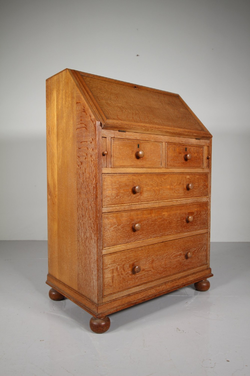 A 1920s oak writing bureau featuring a sloped fall-front desk above four drawers with turned wooden knobs, set on spherical bun feet. View VII