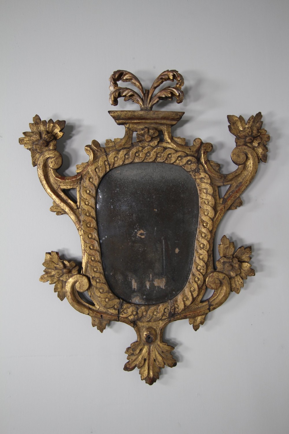 An 18th-century carved wood and gilt wall mirror featuring an ornate cartouche frame with acanthus leaf scrolls, rope twist trim, and a foxed mirror plate.