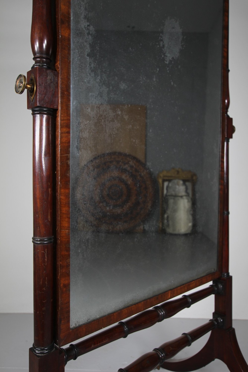 An English Regency mahogany cheval mirror featuring a rectangular tilting glass plate supported by turned uprights and splayed legs with brass paw castors. View V