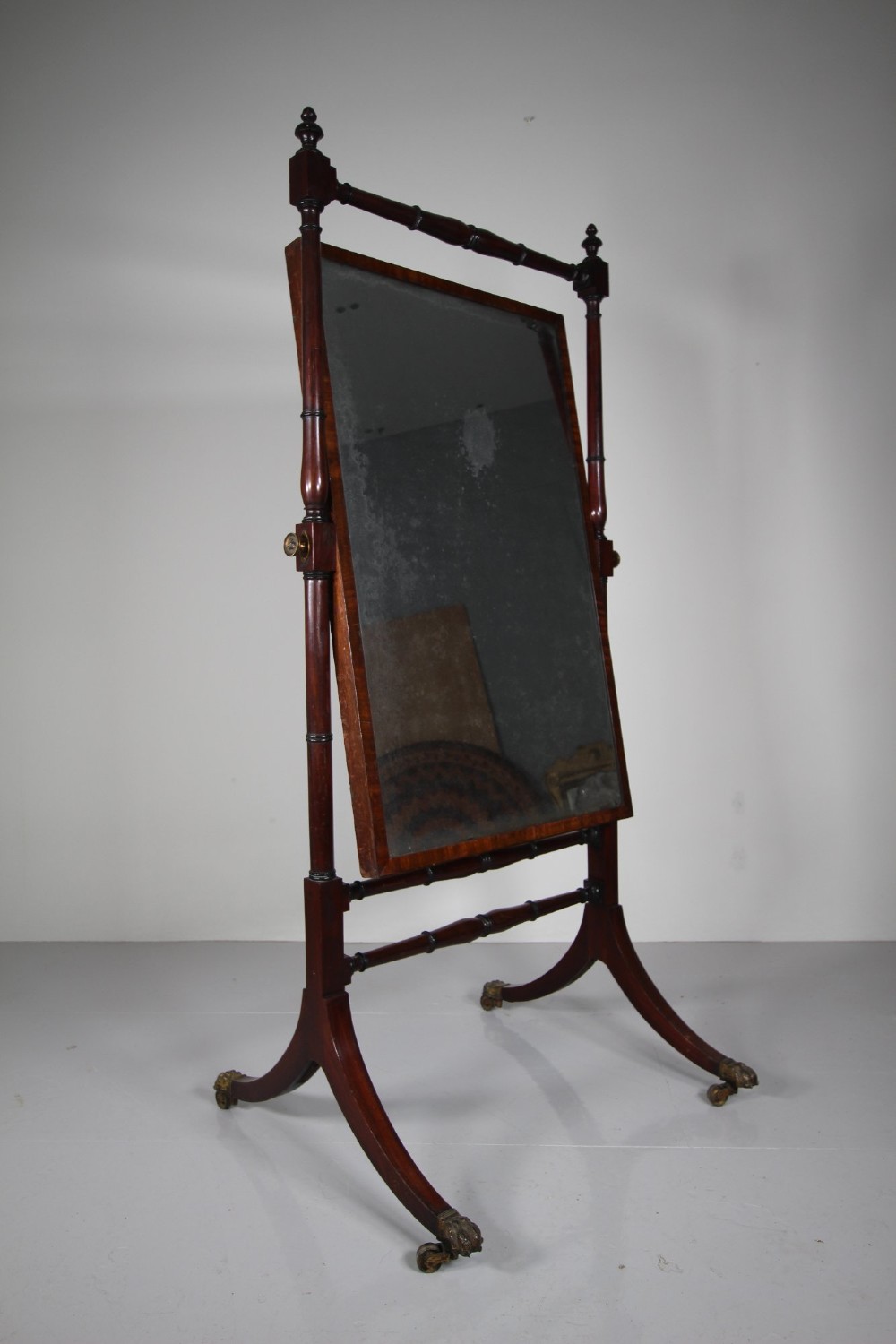 An English Regency mahogany cheval mirror featuring a rectangular tilting glass plate supported by turned uprights and splayed legs with brass paw castors. View VII