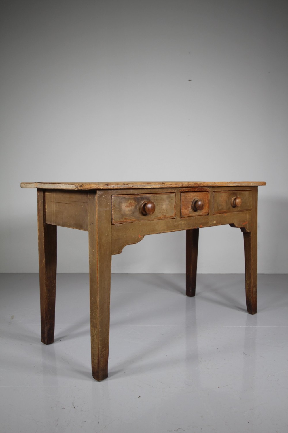 An 18th-century English painted pine serving table featuring three drawers with wooden handles, a shaped apron, and tapered square legs. View VI
