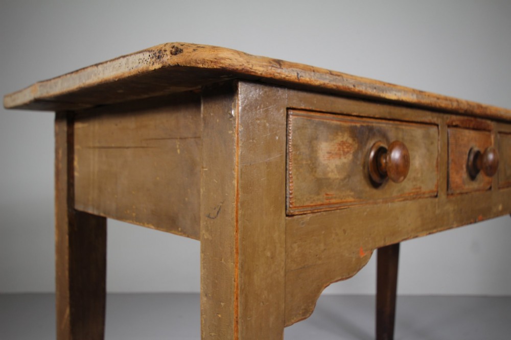 An 18th-century English painted pine serving table featuring three drawers with wooden handles, a shaped apron, and tapered square legs. View VII