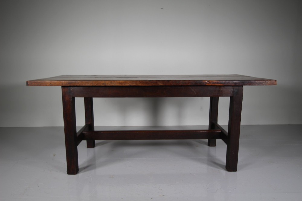 An 18th-century rustic fruitwood dining table featuring a solid plank top and straight square legs joined by a low stretcher base. View VIII
