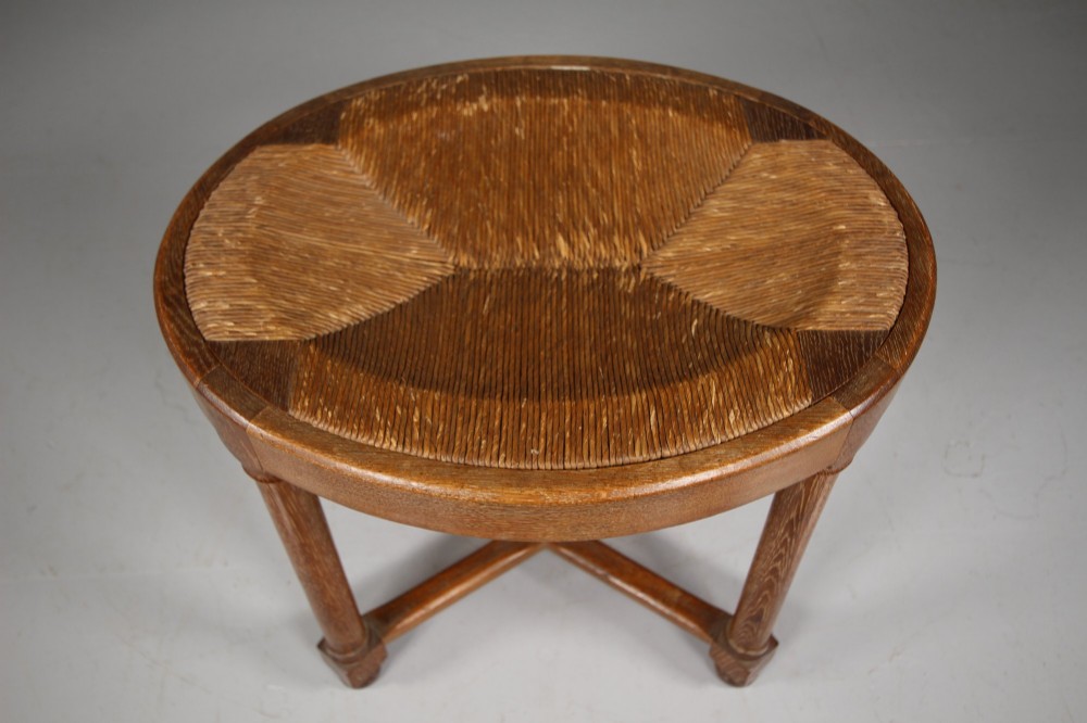 An antique oval oak stool featuring a woven natural rush seat, cylindrical turned legs, and a crossover X-frame stretcher at the base. View V