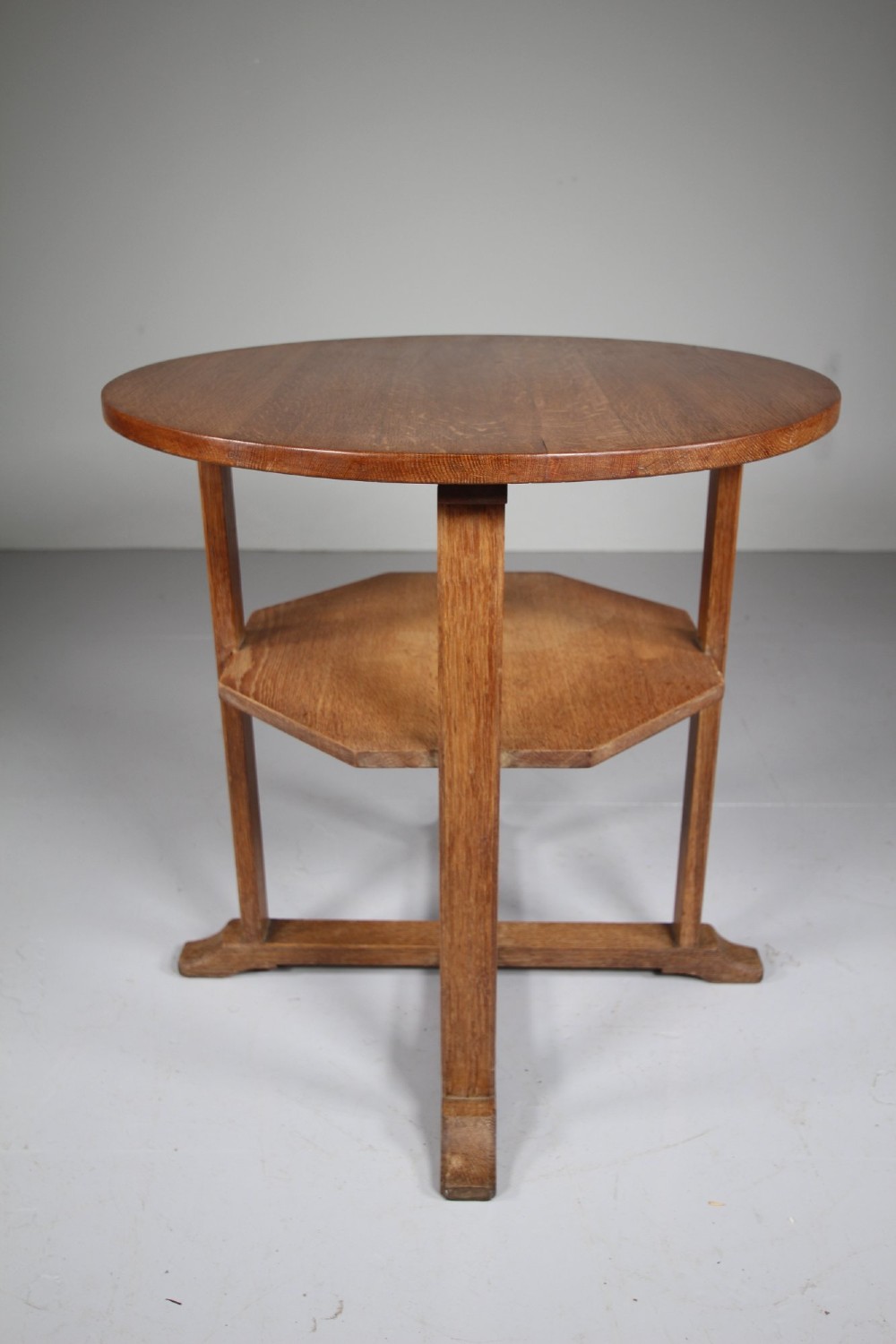 A circular antique oak side table featuring an intermediate lower shelf and an X-frame base stretcher. View III