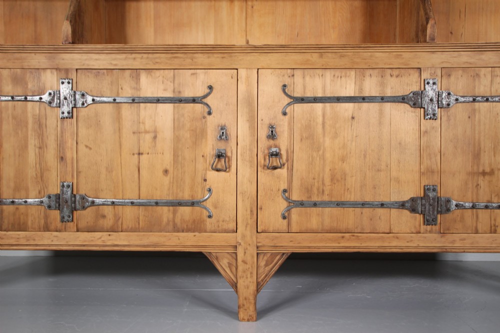 A nineteenth-century pine bookcase featuring a three-bay open top section with adjustable shelving set upon a lower cabinet with four panelled doors adorned with wrought iron strap hinges. View II