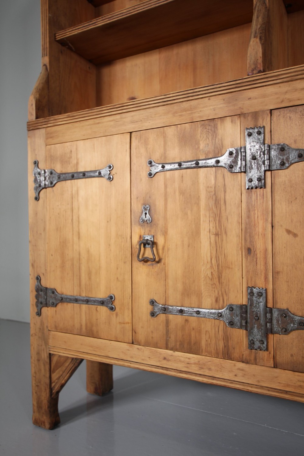 A nineteenth-century pine bookcase featuring a three-bay open top section with adjustable shelving set upon a lower cabinet with four panelled doors adorned with wrought iron strap hinges. View III