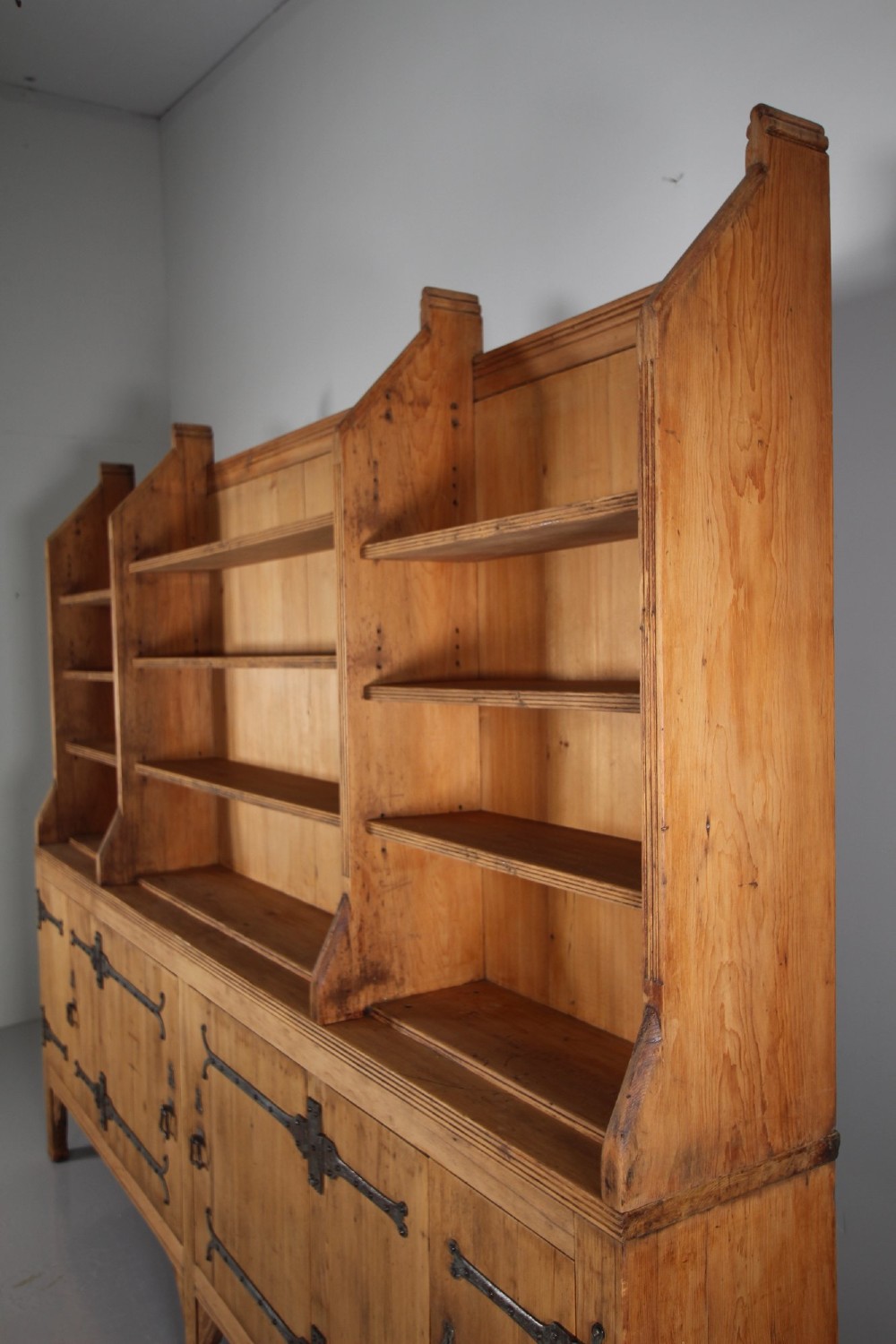 A nineteenth-century pine bookcase featuring a three-bay open top section with adjustable shelving set upon a lower cabinet with four panelled doors adorned with wrought iron strap hinges. View IV