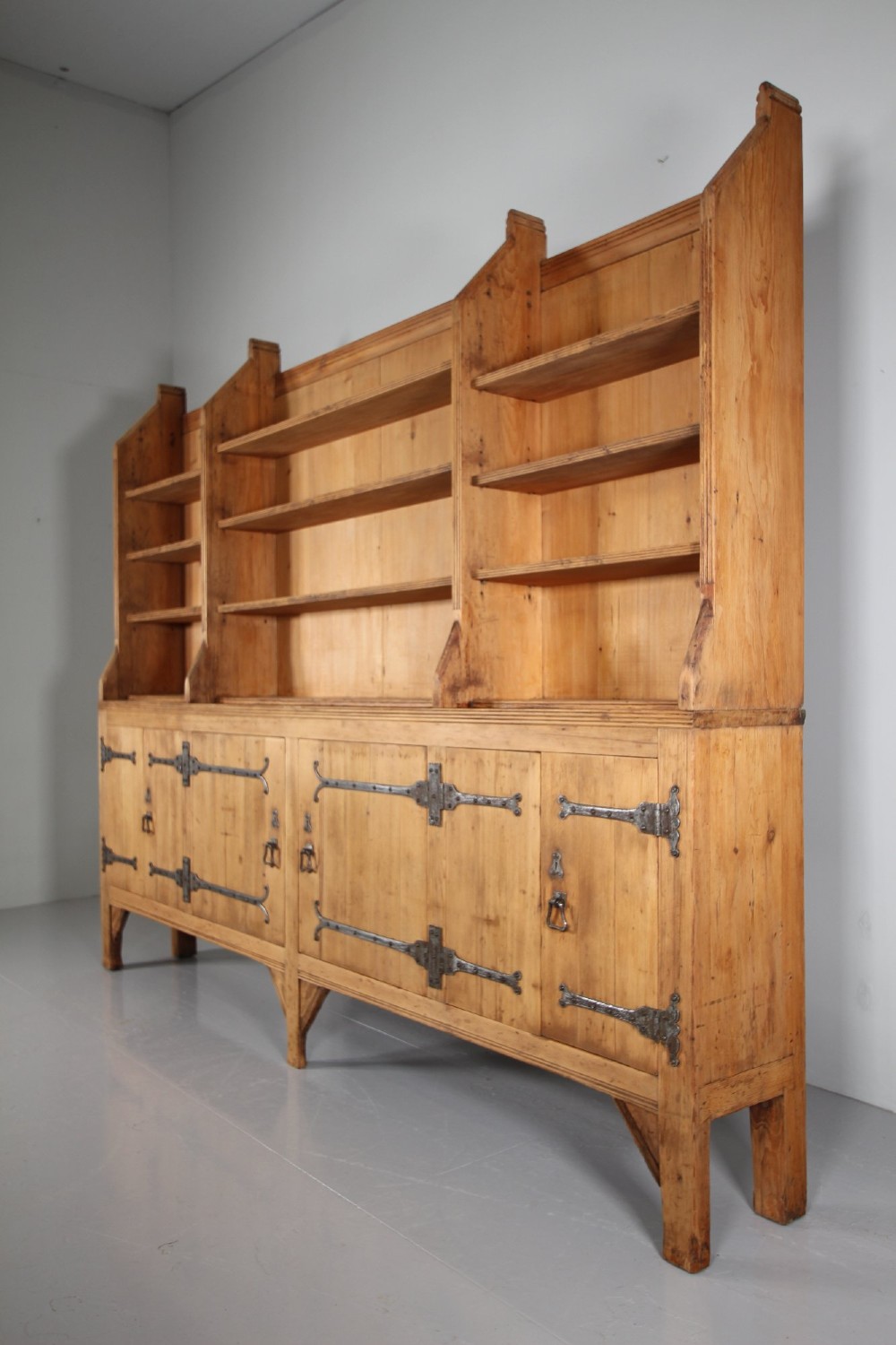 A nineteenth-century pine bookcase featuring a three-bay open top section with adjustable shelving set upon a lower cabinet with four panelled doors adorned with wrought iron strap hinges. View V