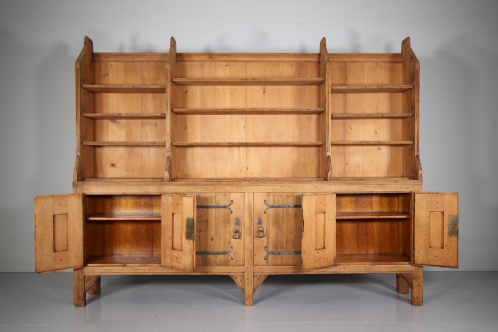 A nineteenth-century pine bookcase featuring a three-bay open top section with adjustable shelving set upon a lower cabinet with four panelled doors adorned with wrought iron strap hinges. View VI