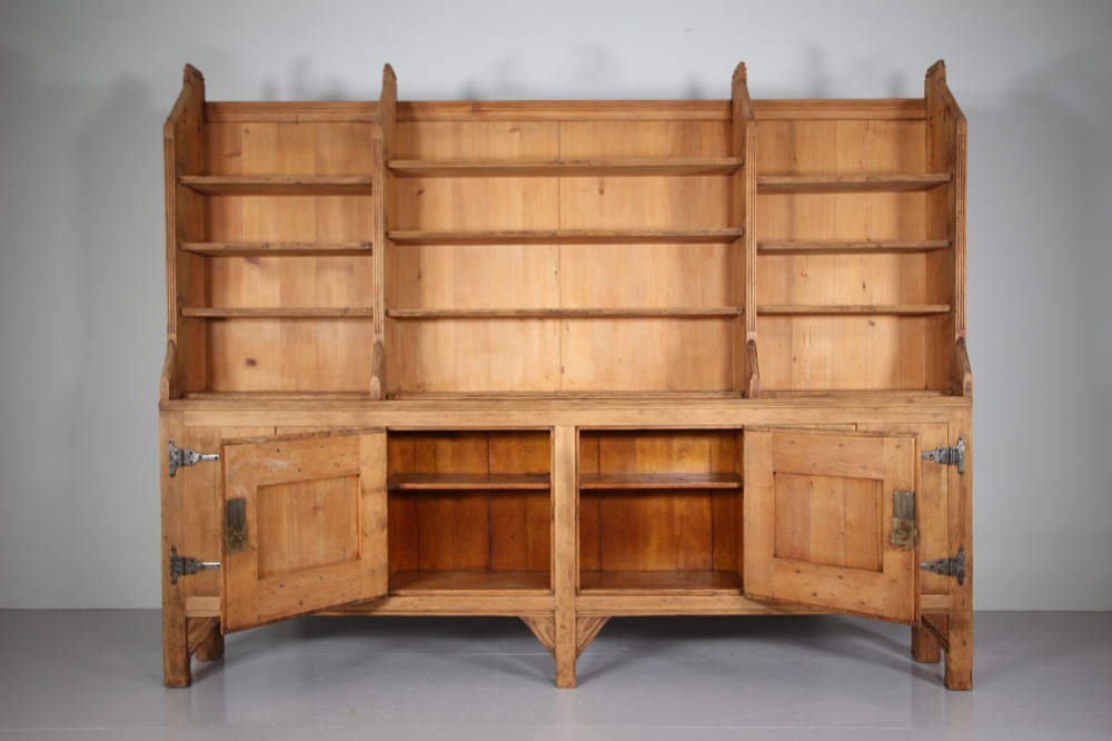 A nineteenth-century pine bookcase featuring a three-bay open top section with adjustable shelving set upon a lower cabinet with four panelled doors adorned with wrought iron strap hinges. View VII