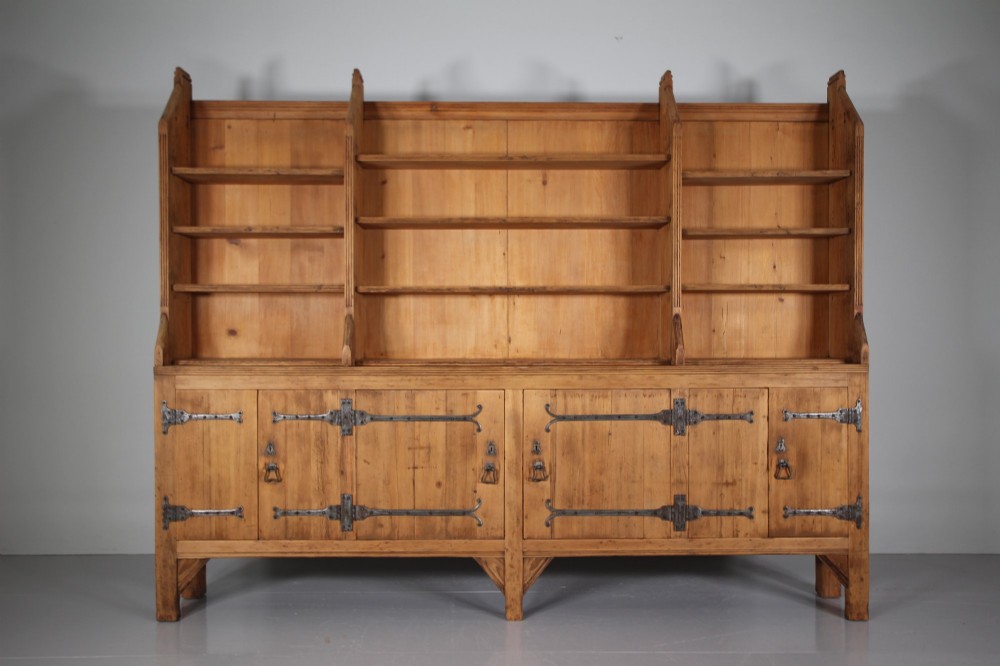 A nineteenth-century pine bookcase featuring a three-bay open top section with adjustable shelving set upon a lower cabinet with four panelled doors adorned with wrought iron strap hinges. View VIII