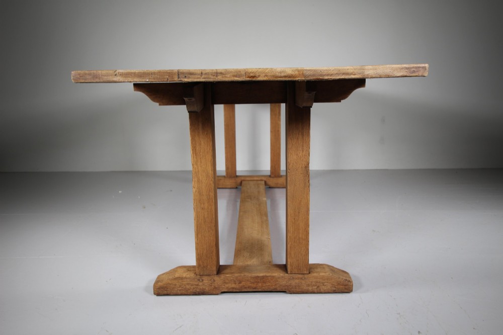 A 1930s solid oak refectory dining table featuring a rectangular top set over double column trestle ends and a low central stretcher. View II