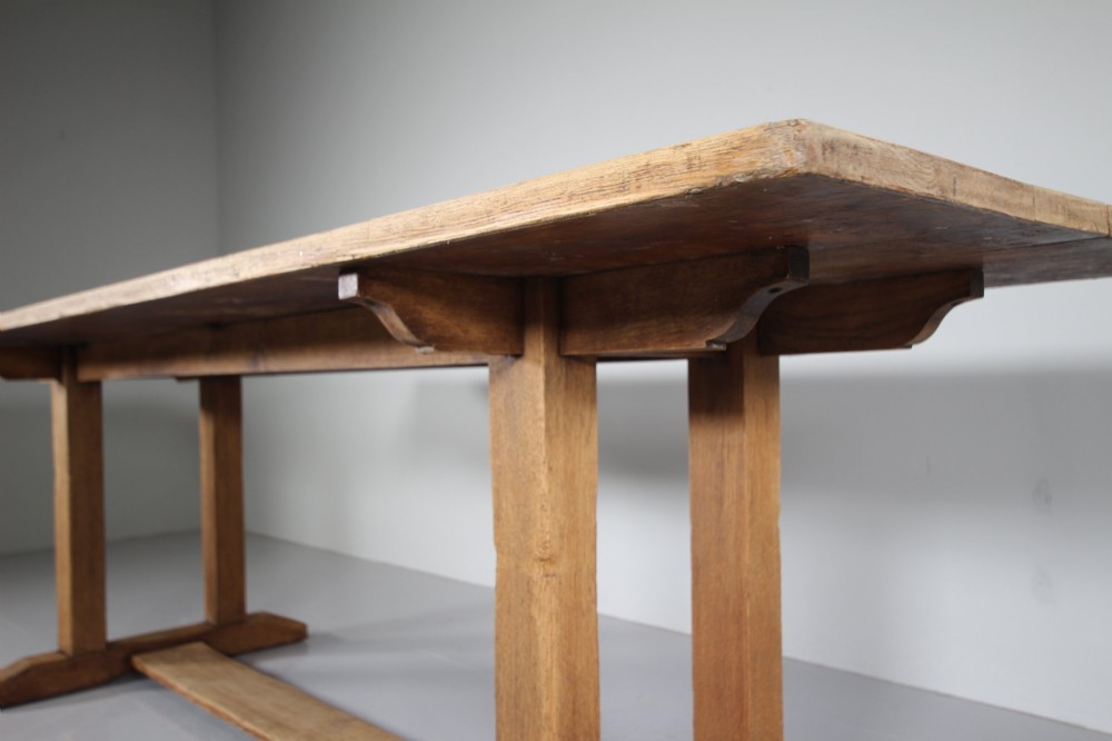 A 1930s solid oak refectory dining table featuring a rectangular top set over double column trestle ends and a low central stretcher. View VI