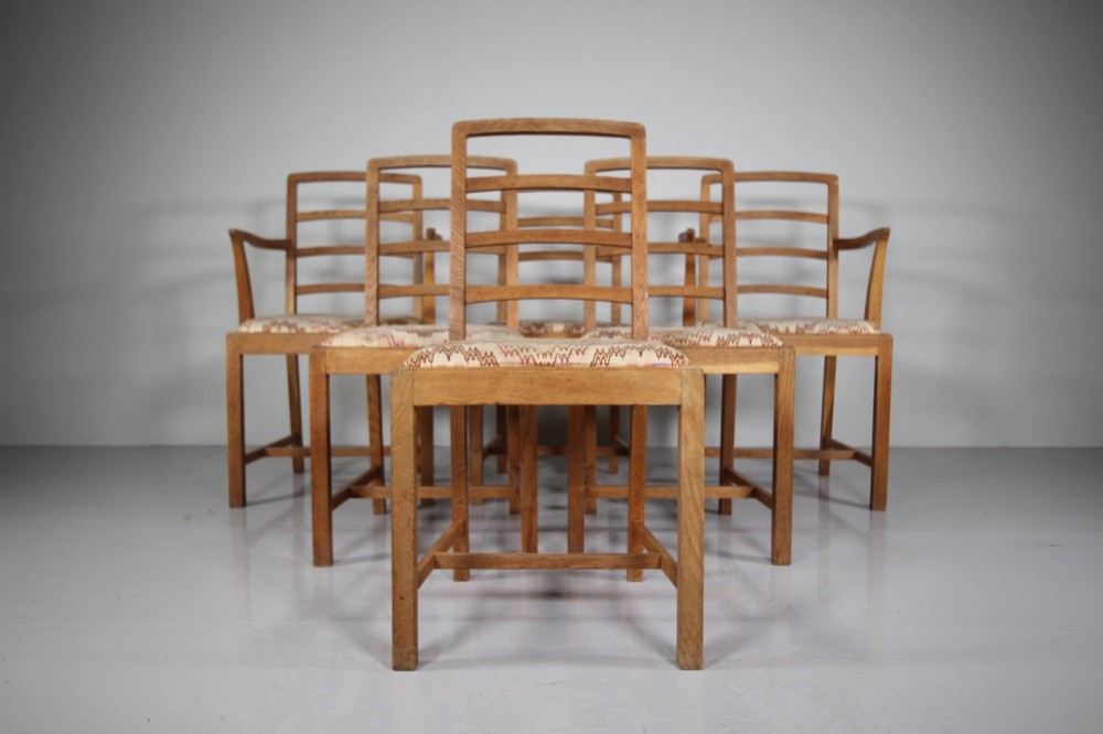 A set of six 1920s oak dining chairs including two armchairs, featuring structured horizontal ladder backs and patterned fabric upholstered seats.