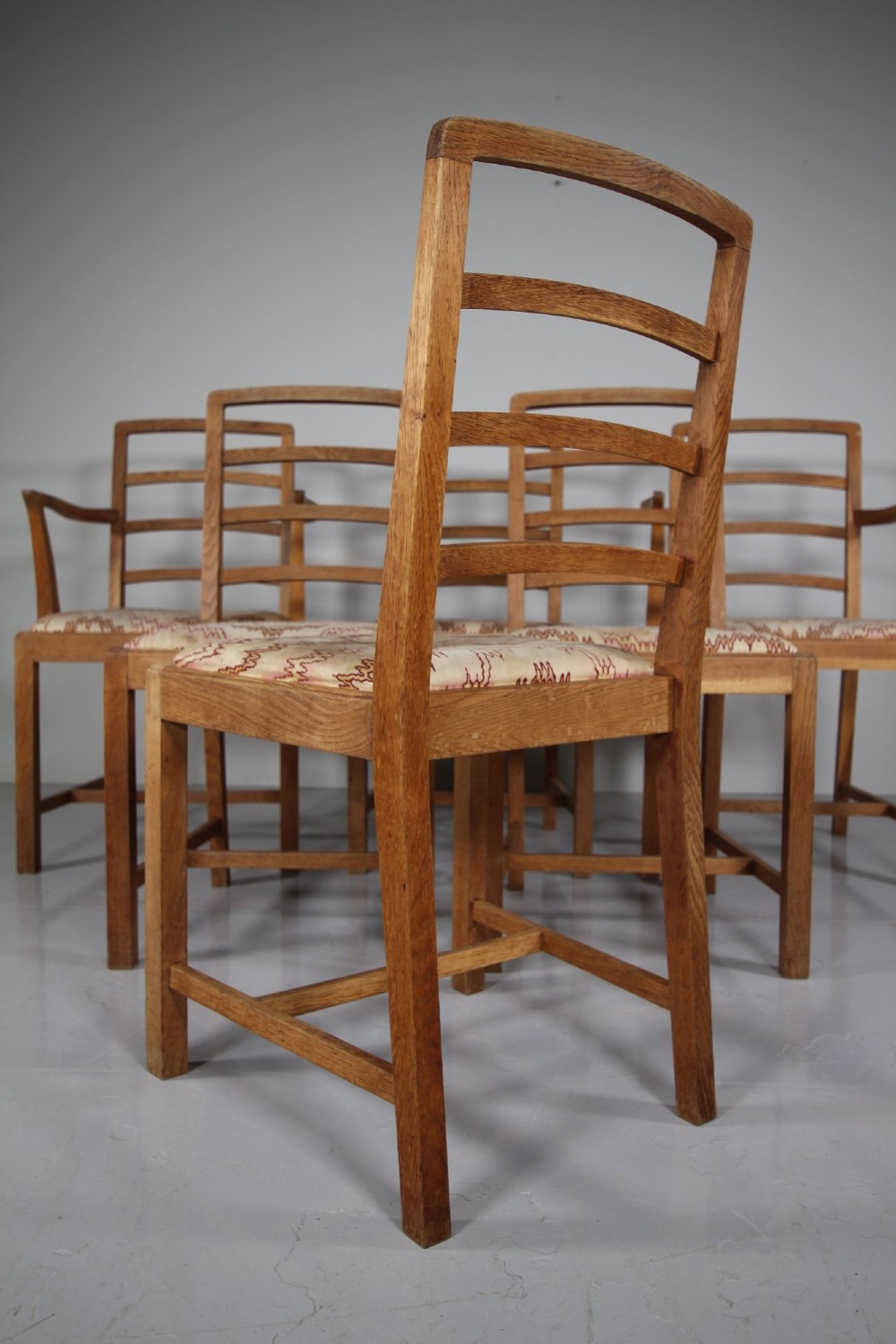 A set of six 1920s oak dining chairs including two armchairs, featuring structured horizontal ladder backs and patterned fabric upholstered seats. View V