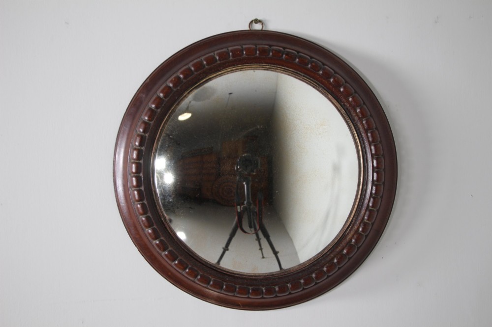 A circular antique convex wall mirror set within a dark carved oak frame featuring a beaded border and a brass hanging ring. View II