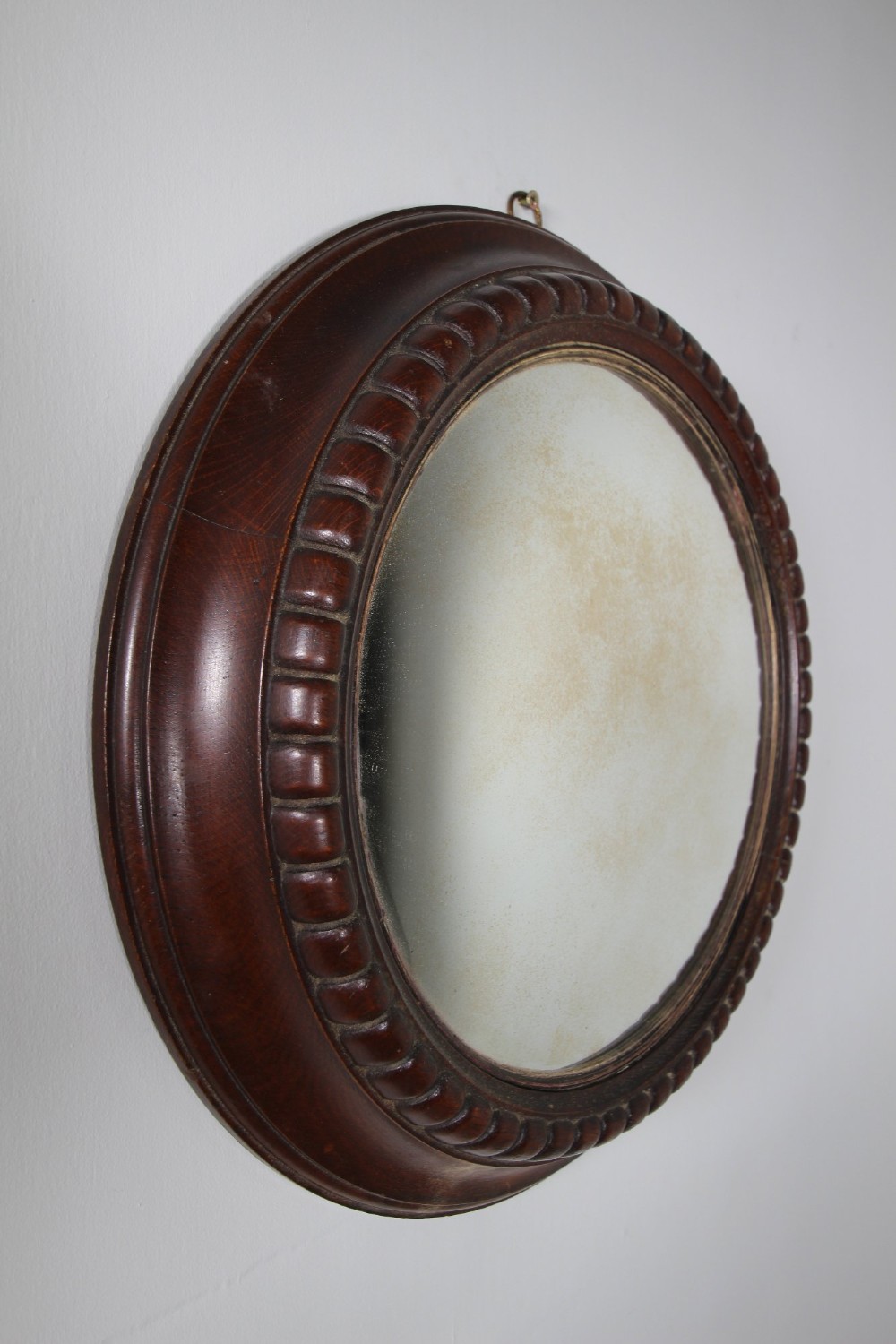 A circular antique convex wall mirror set within a dark carved oak frame featuring a beaded border and a brass hanging ring. View III