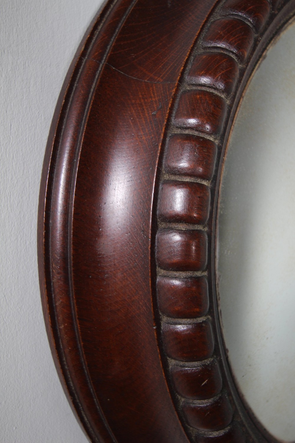 A circular antique convex wall mirror set within a dark carved oak frame featuring a beaded border and a brass hanging ring. View IV