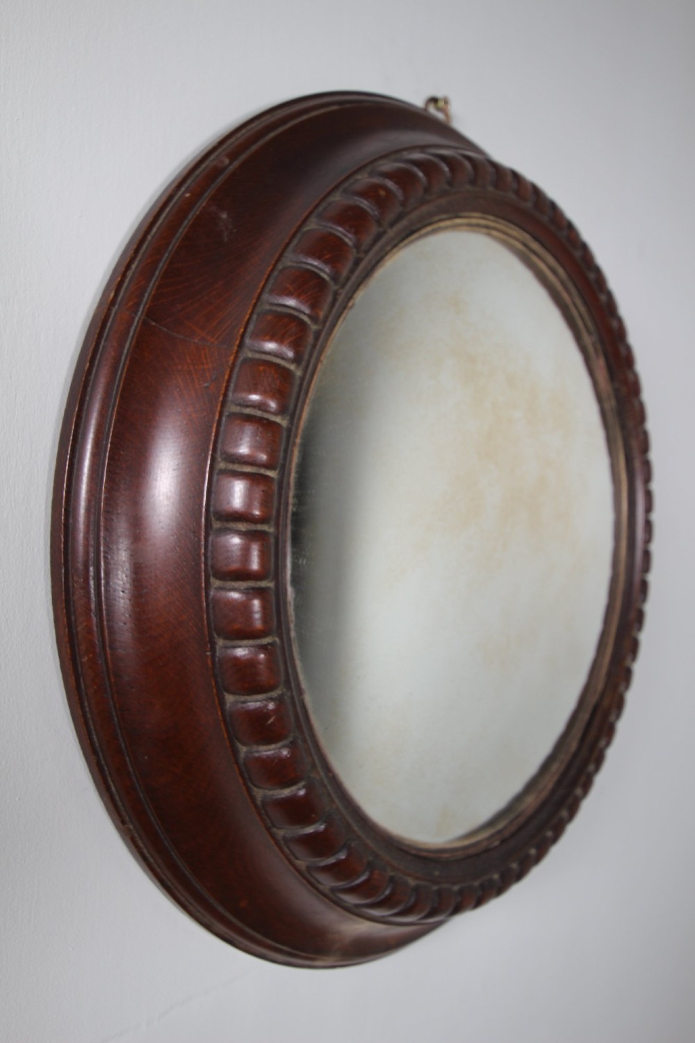 A circular antique convex wall mirror set within a dark carved oak frame featuring a beaded border and a brass hanging ring. View V