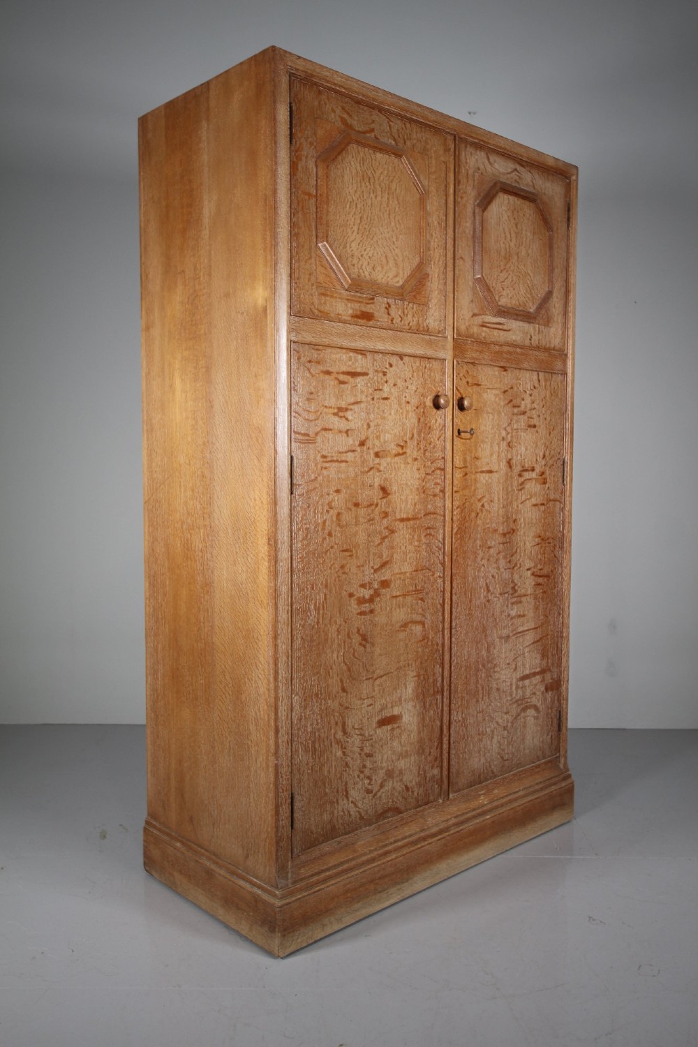 A tall light oak two-door wardrobe featuring octagonal upper panels, quarter-sawn wood grain, and small turned knobs on a plinth base.