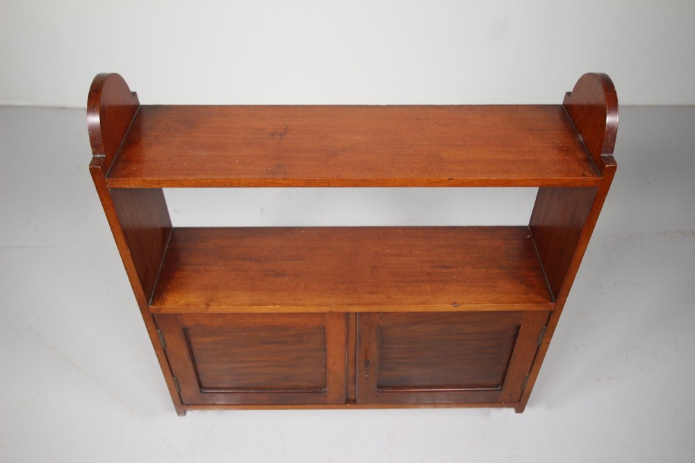 An Arts and Crafts walnut wall cabinet with an open top shelf above twin panelled cupboard doors and rounded side panels. View II