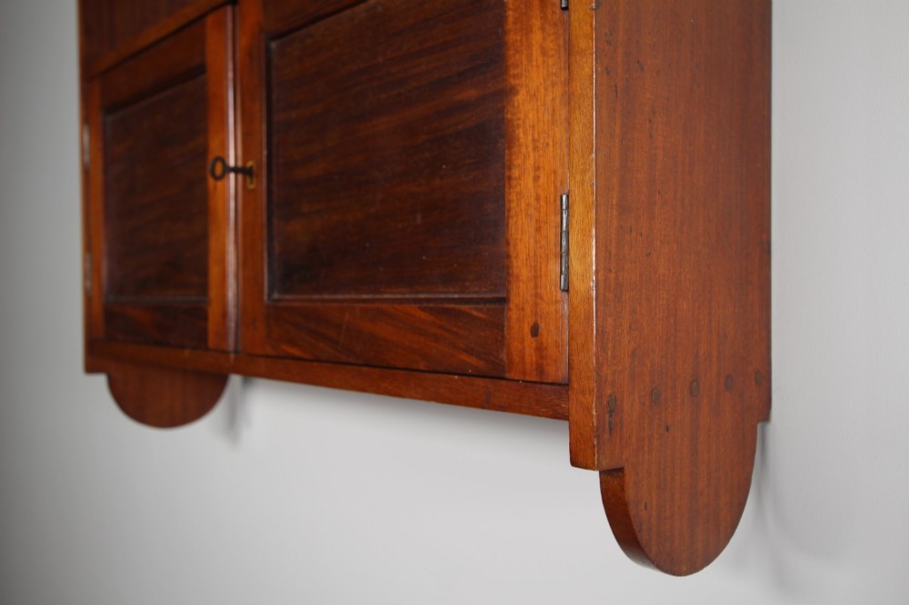 An Arts and Crafts walnut wall cabinet with an open top shelf above twin panelled cupboard doors and rounded side panels. View IV