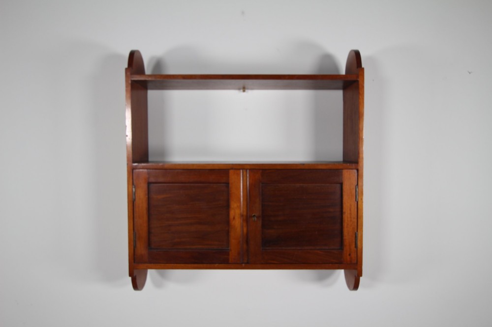An Arts and Crafts walnut wall cabinet with an open top shelf above twin panelled cupboard doors and rounded side panels. View V