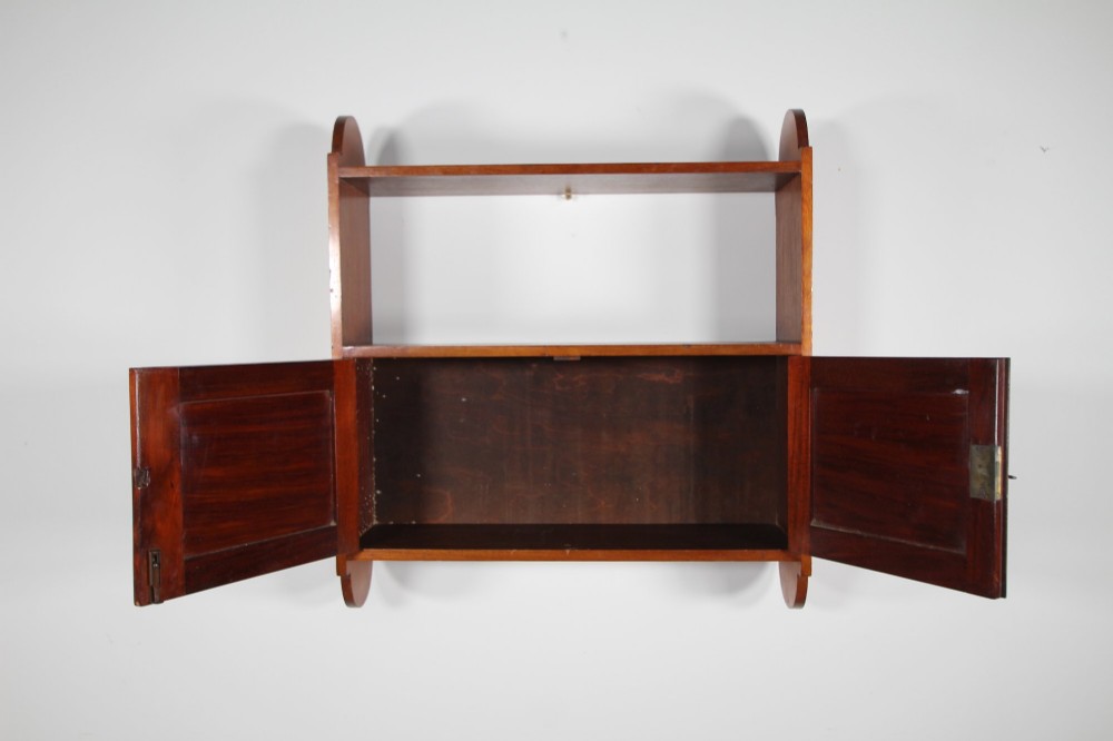 An Arts and Crafts walnut wall cabinet with an open top shelf above twin panelled cupboard doors and rounded side panels. View VI