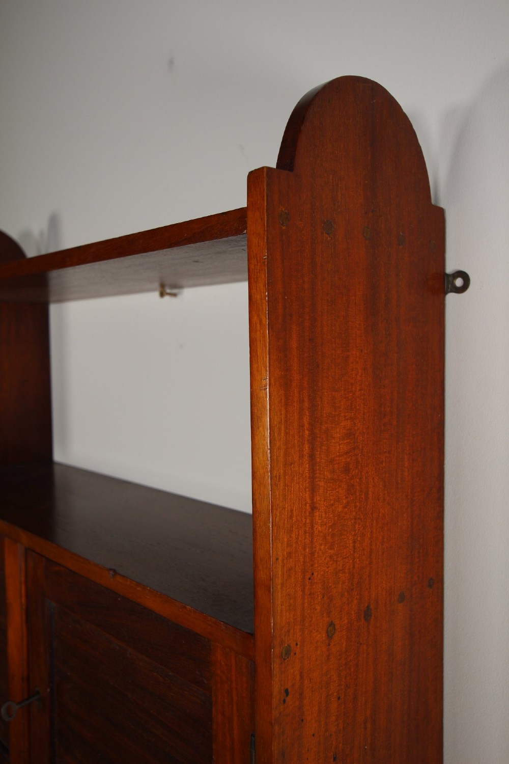 An Arts and Crafts walnut wall cabinet with an open top shelf above twin panelled cupboard doors and rounded side panels. View VIII
