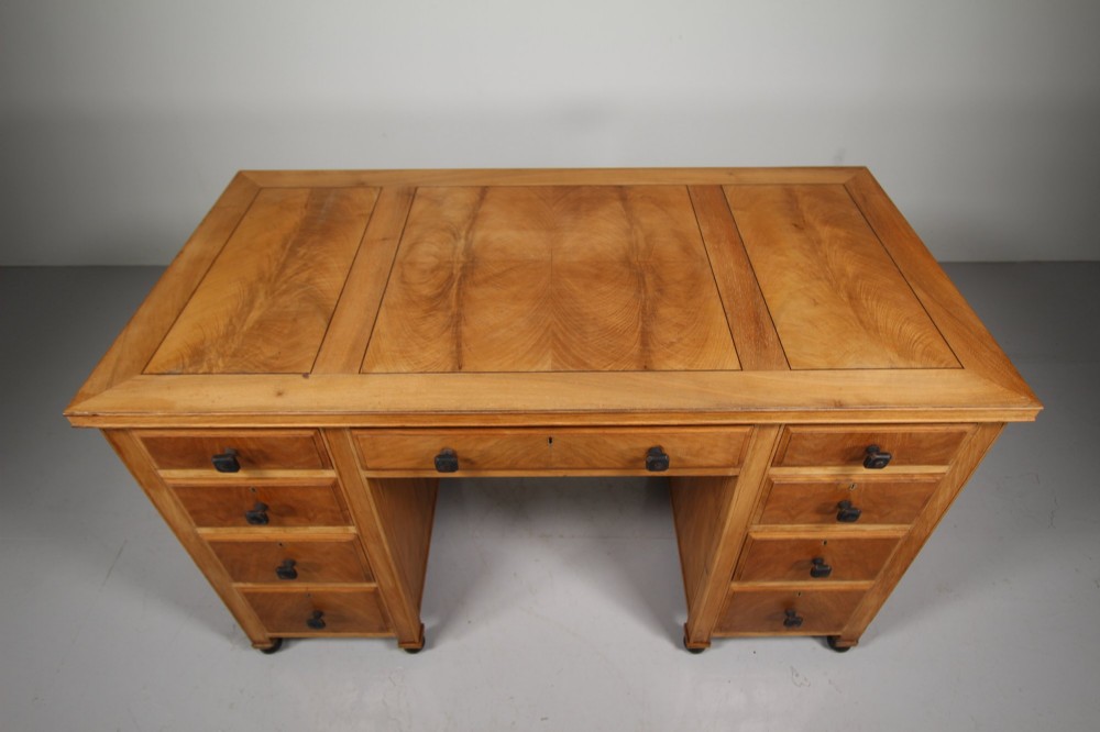 A light oak kneehole writing desk with nine drawers featuring square ebonised handles and ebonised ball feet. View V