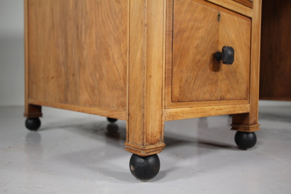 A light oak kneehole writing desk with nine drawers featuring square ebonised handles and ebonised ball feet. View X