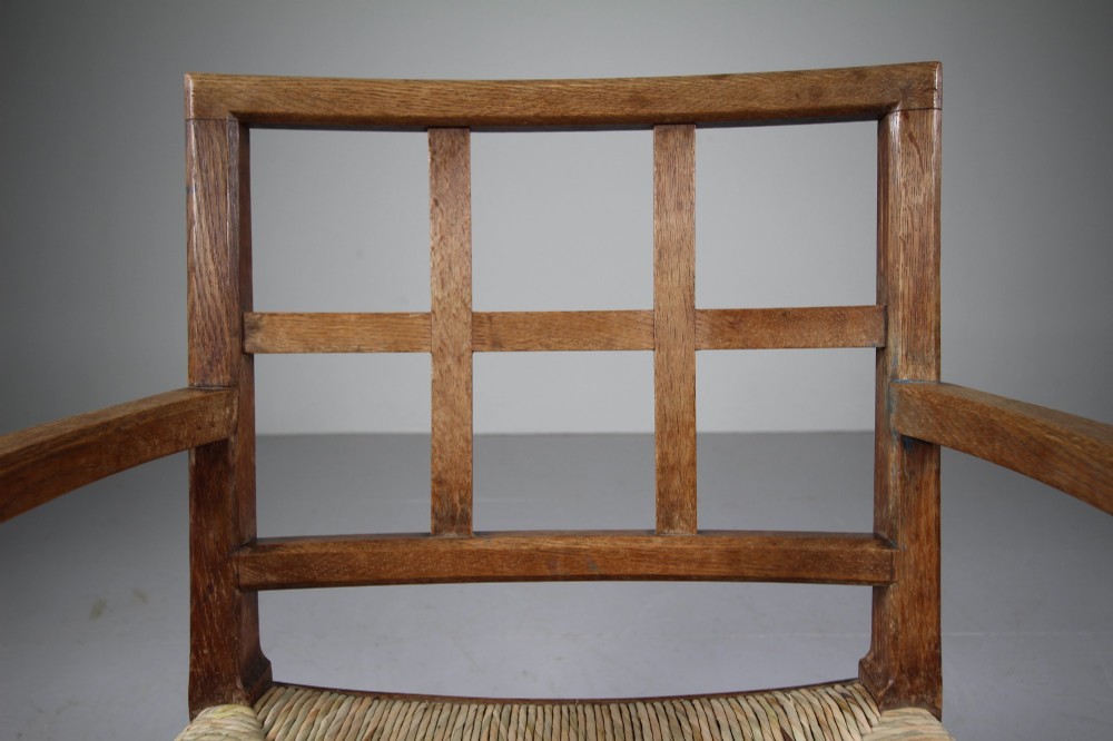 An Arts and Crafts oak fireside chair featuring a grid backrest, wide flat armrests, a woven rush seat, and a sledge base. View III