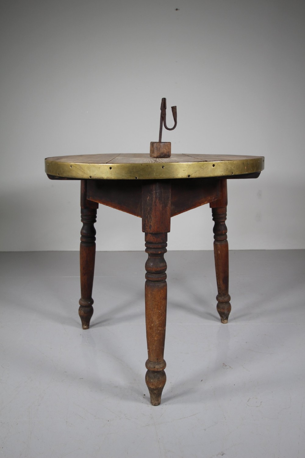 An early nineteenth-century wooden cricket table featuring a circular plank top with a brass-bound rim supported on three turned legs. View II
